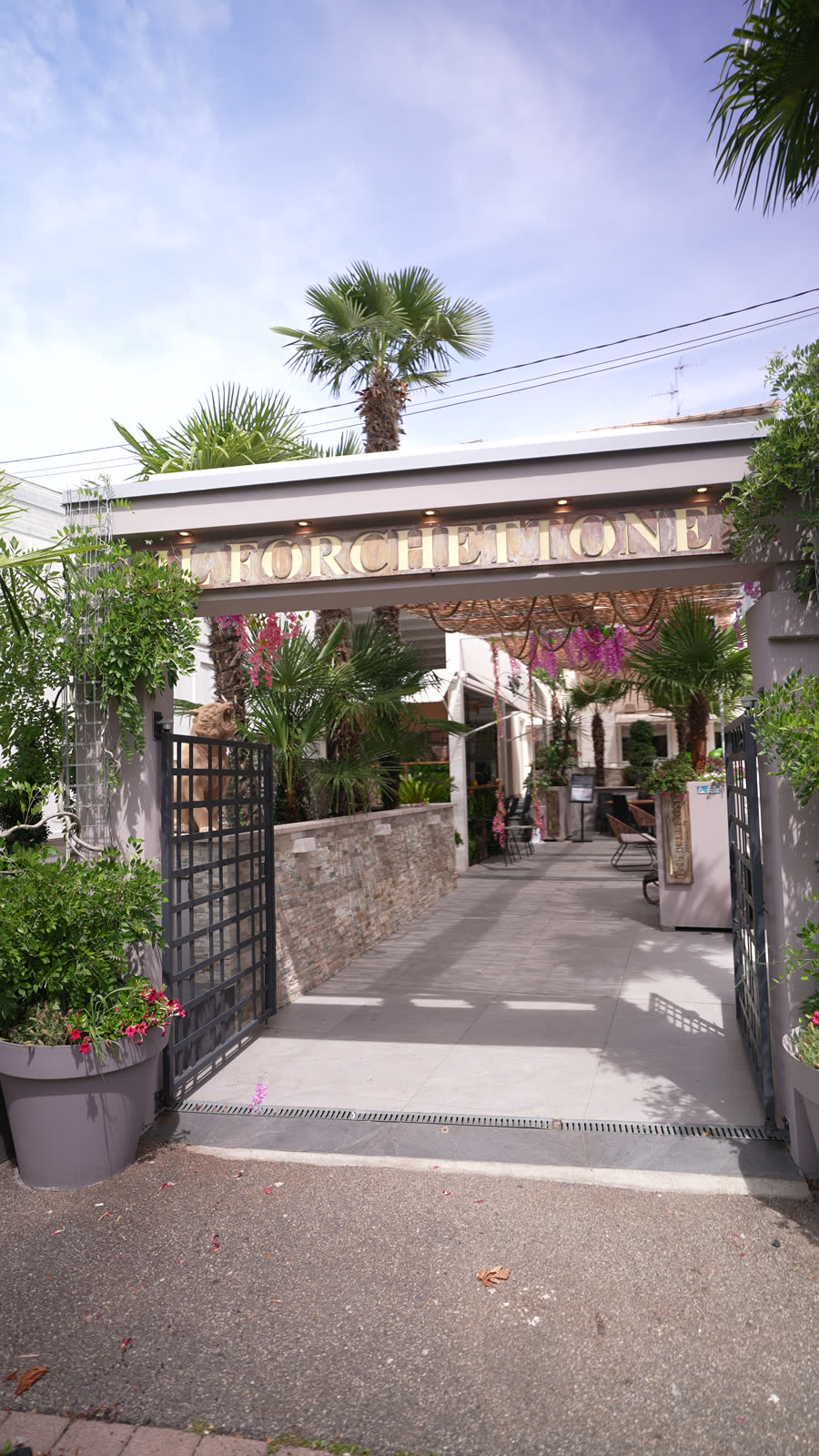 L’entrée du restaurant Il Forchettone sous les palmiers, lettres dorées au-dessus du portail