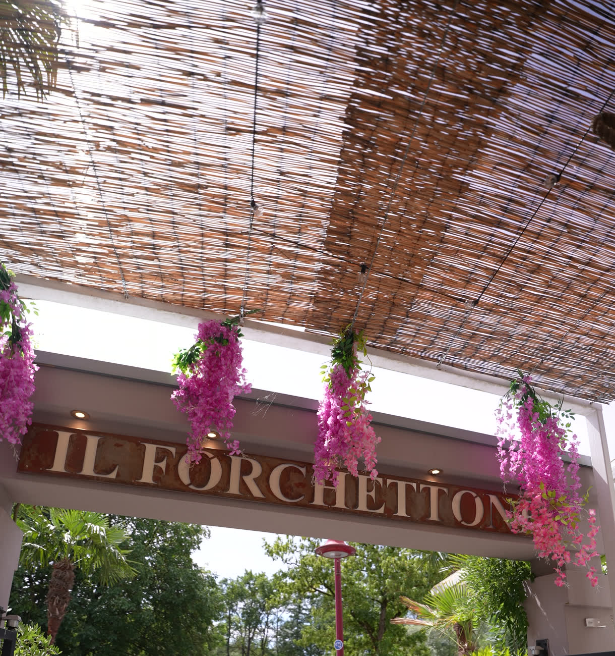 Le porche du restaurant&nbsp;: glycines roses, toit de roseaux et lettres Il Forchettone
